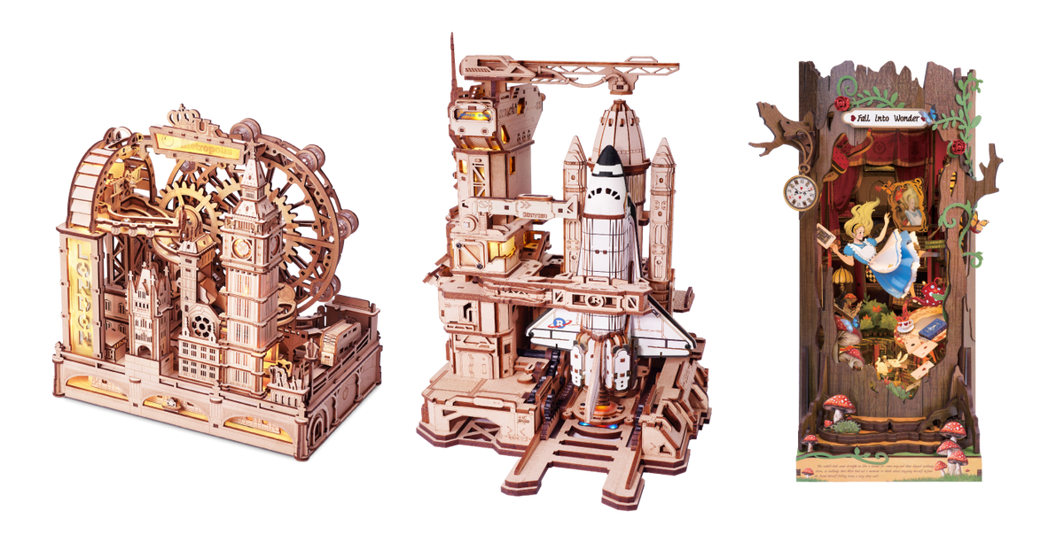 Three wooden model kits shown together including a carousel, castle tower and Alice in Wonderland plaque