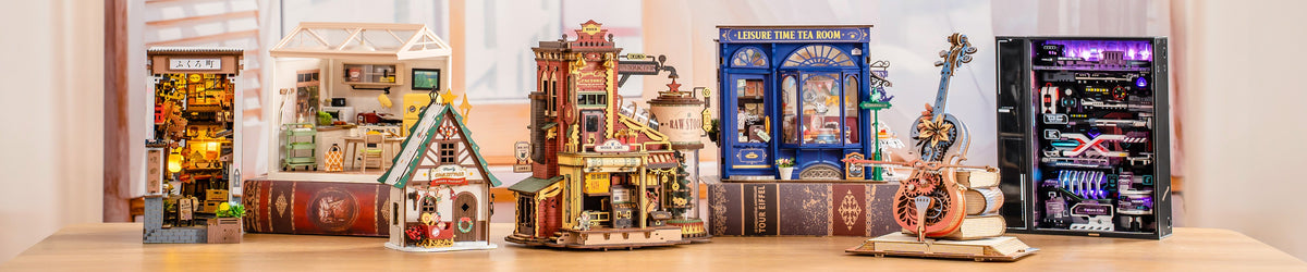 Wide banner showing six Rolife and ROKR book nook and miniature models in a row on a wooden table including a lit Japanese alley, greenhouse, steampunk tower, tea room, violin, and server rack