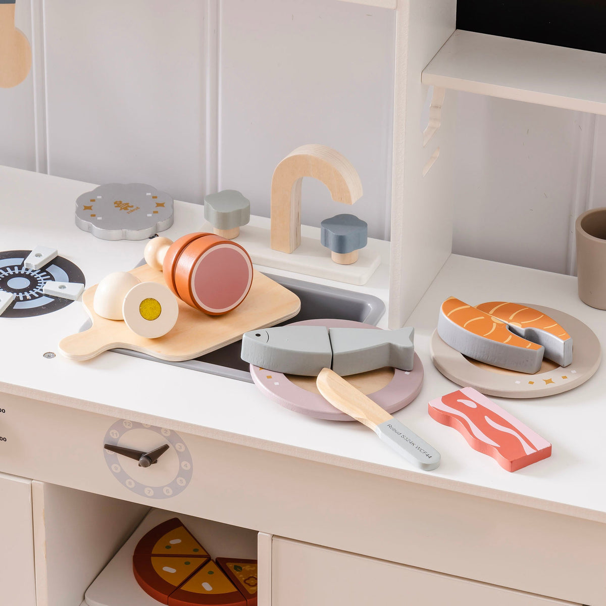 ROBUD wooden meat cutting set arranged on a white play kitchen counter with salmon steak on plate, egg, chicken leg, bacon, grey fish, and wooden knife