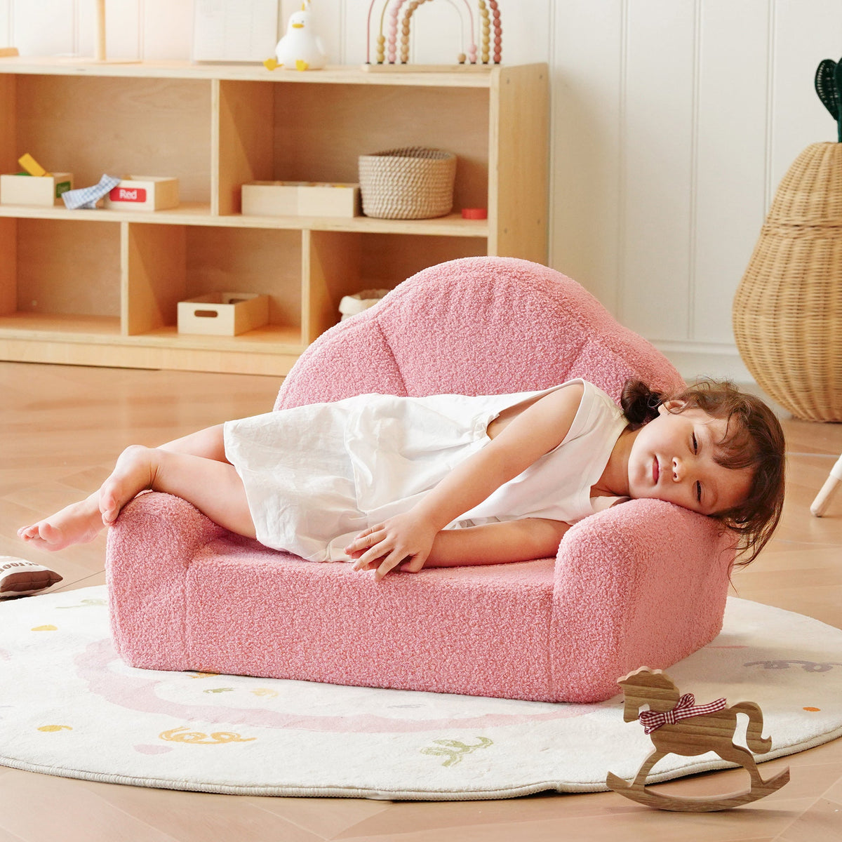 Child lying on the ROBUD pink Children's Sofa with a small rocking horse visible in background