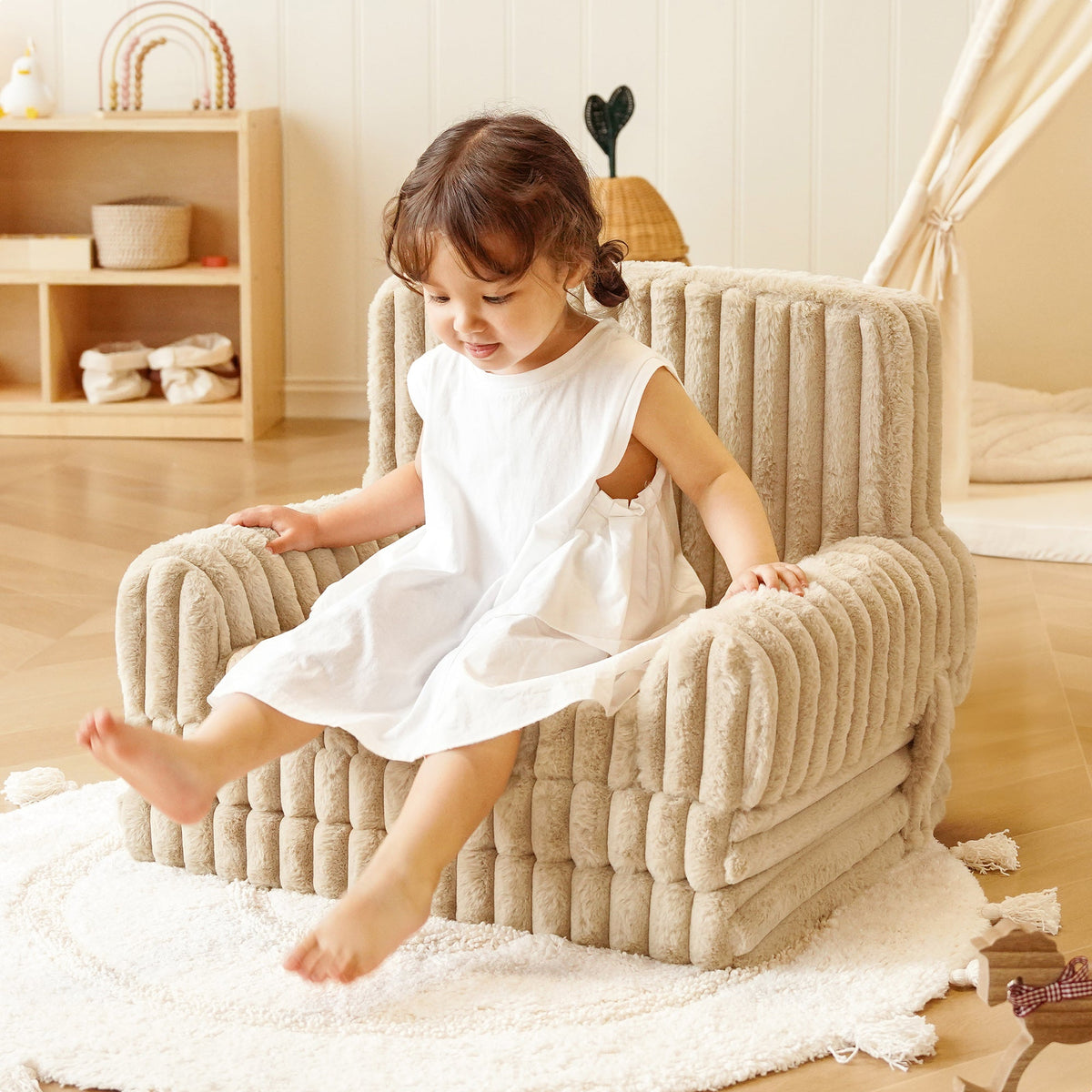 Toddler girl in white dress sitting on ROBUD Children's Sofa beige corduroy armchair on a cream rug in a sunlit nursery room