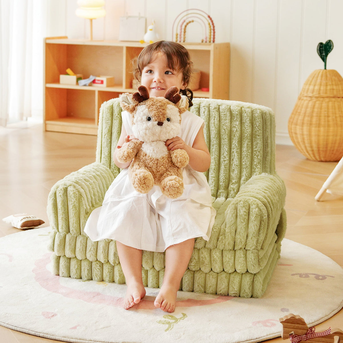 Toddler girl seated in a ROBUD green striped armchair hugging a plush giraffe toy in a cozy children's bedroom.