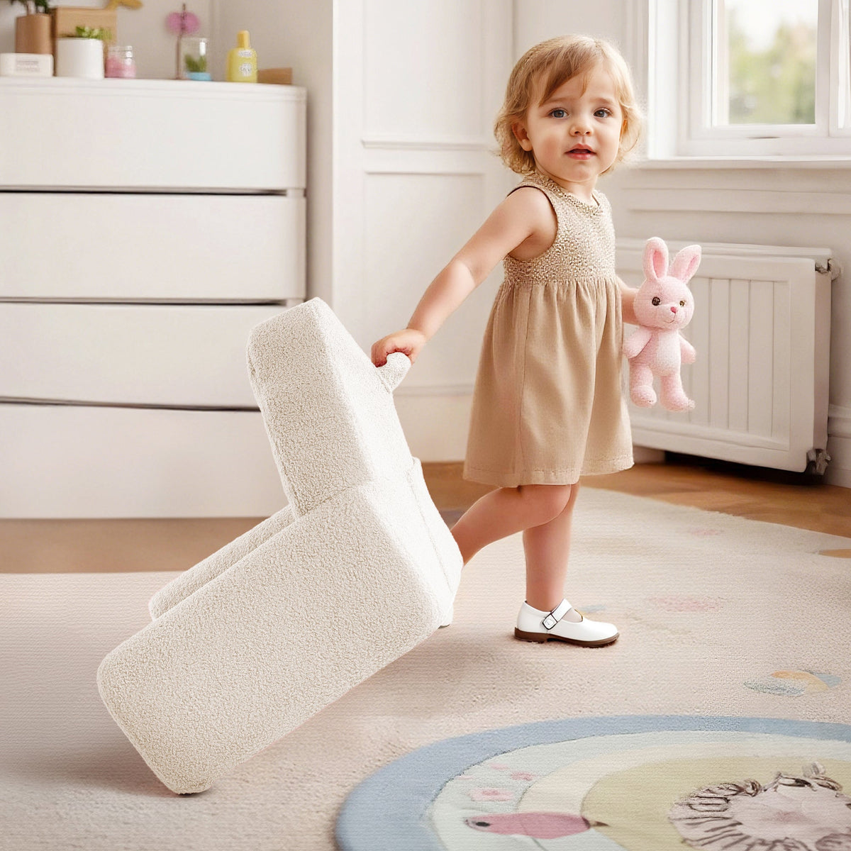 Toddler girl carrying the ROBUD cream children's sofa cushion across a playroom holding a stuffed rabbit