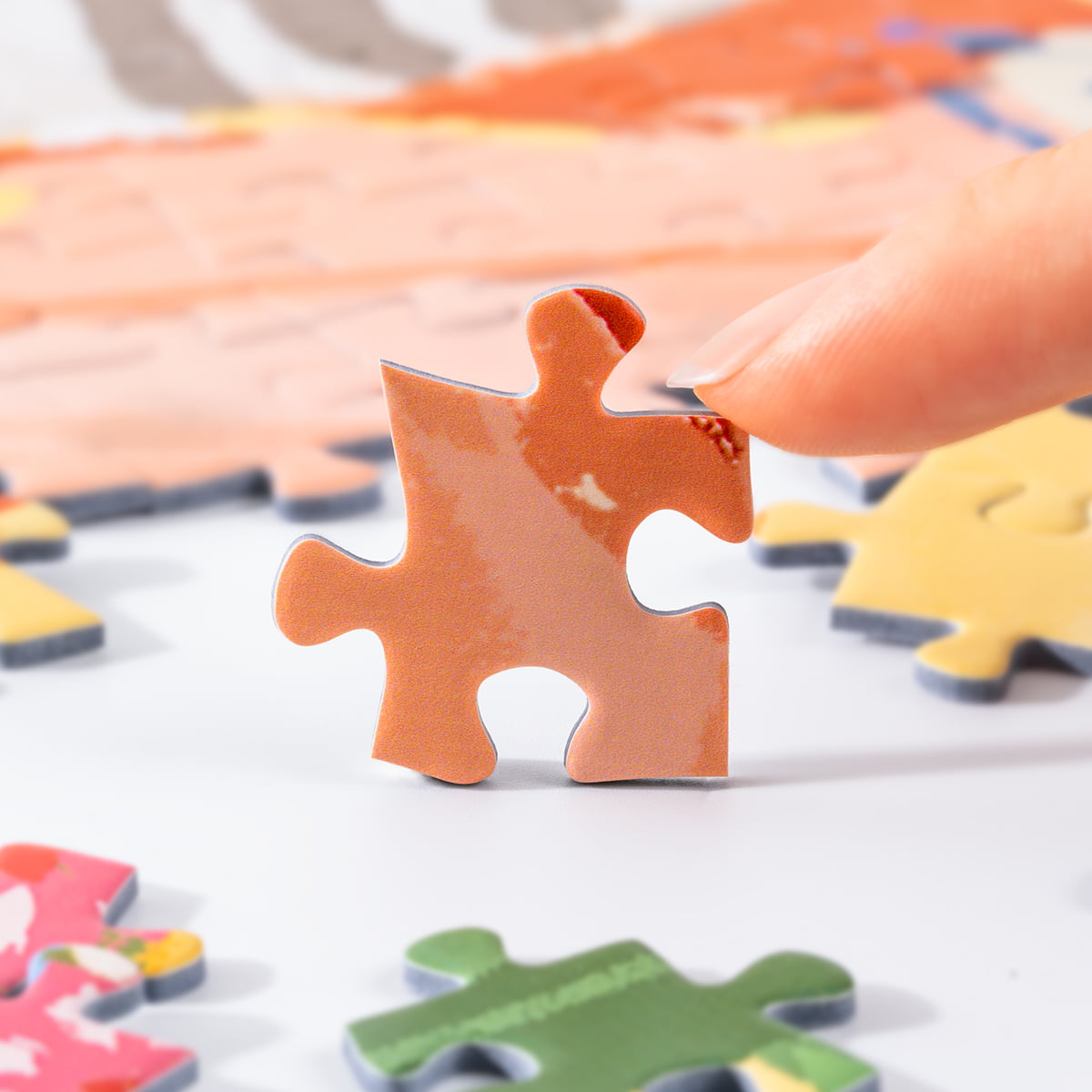 Close-up of a Rolife Leisurely Holiday PT002 puzzle piece held above the spread showing illustrated pastel peach tones