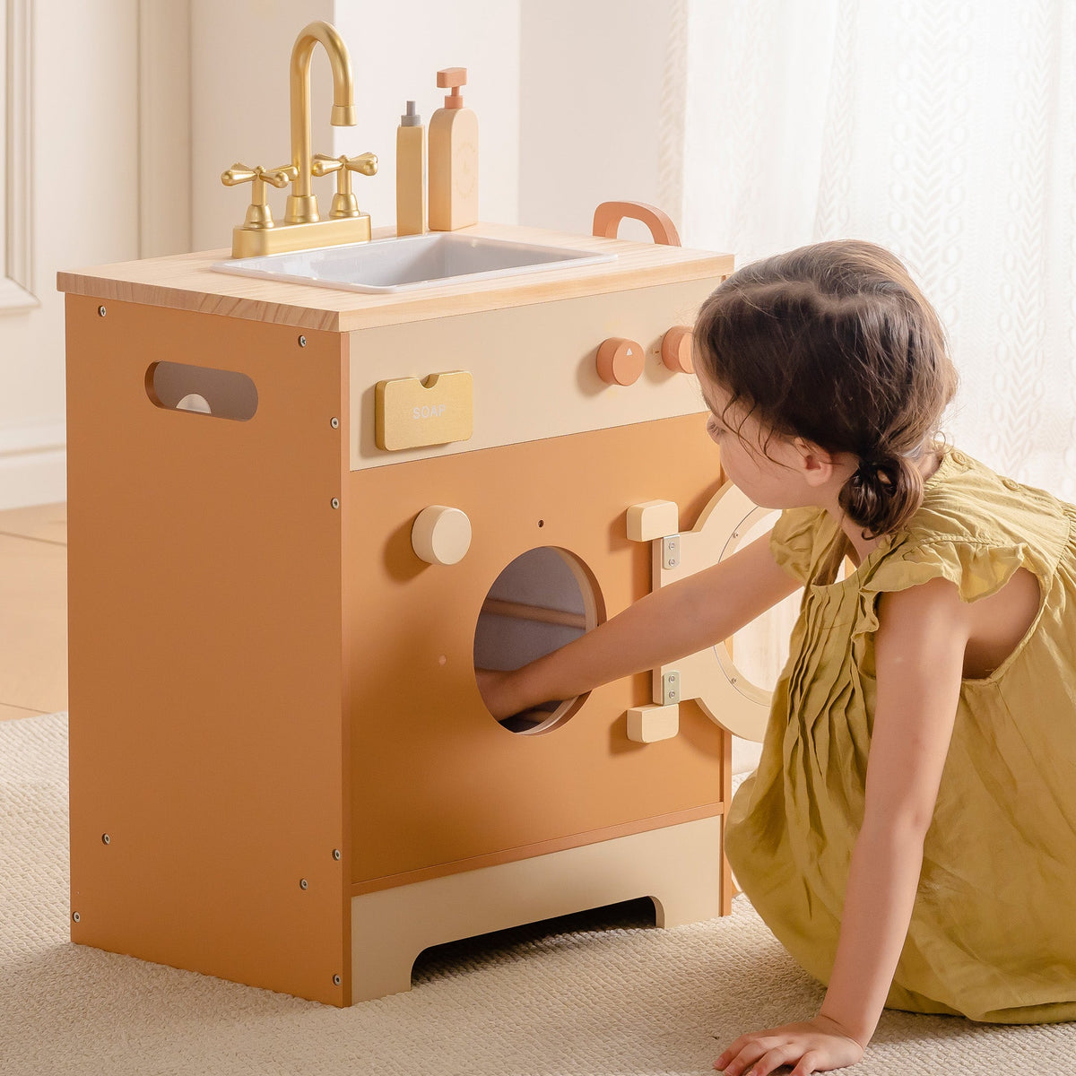 Young girl crouching to open the round porthole of ROBUD Wooden Caramel Laundry Washer with brass faucet sink on top
