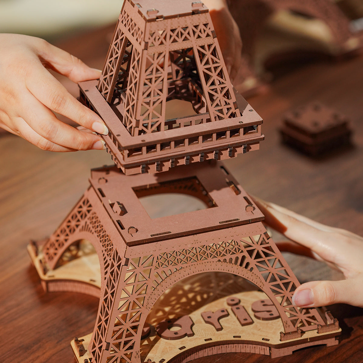 Two hands pressing an upper lattice section onto the mid-level structure of the Rolife Eiffel Tower model during assembly