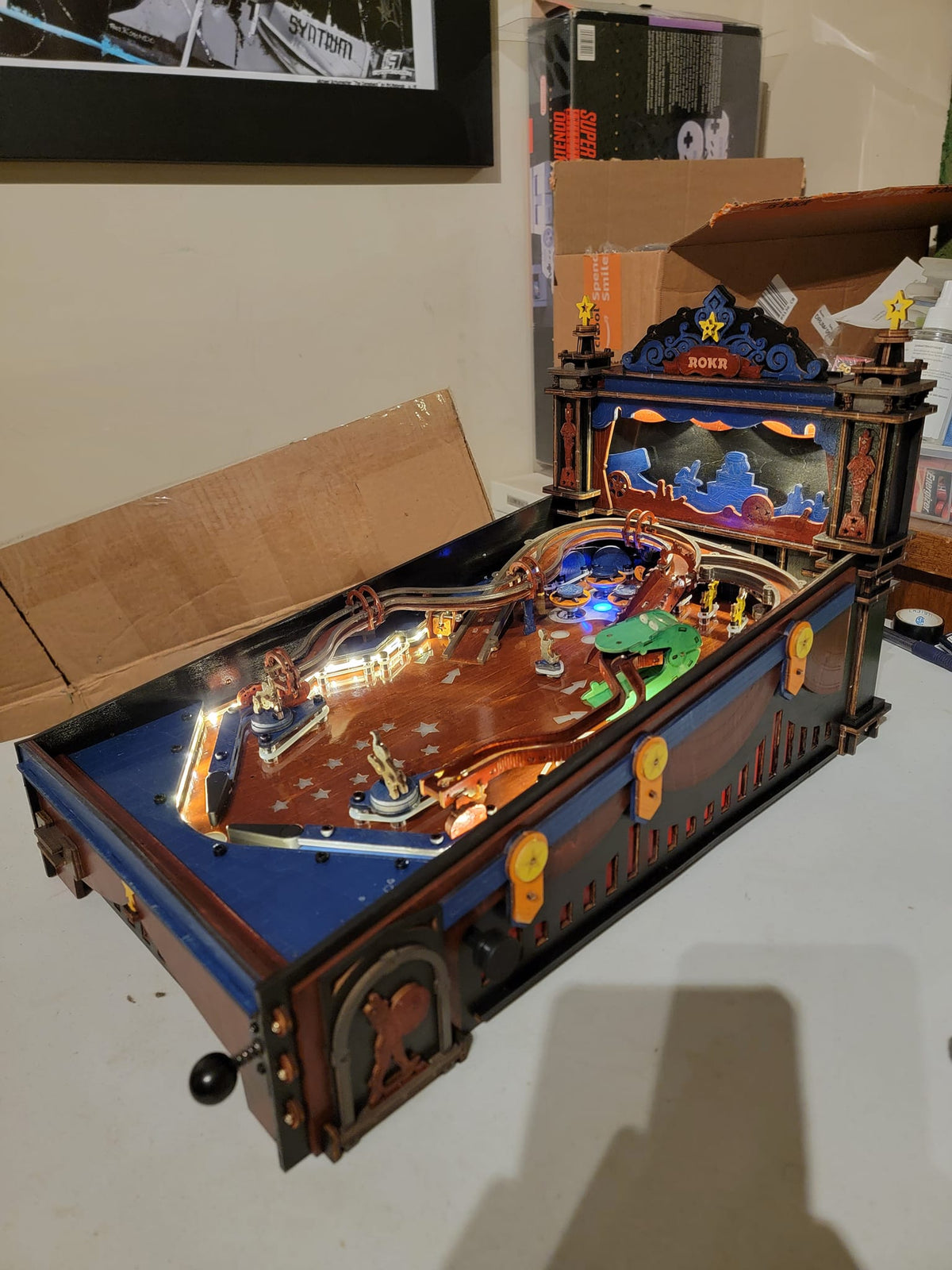 Robotime blue pinball table model sits on a shelf with a raised backboard.