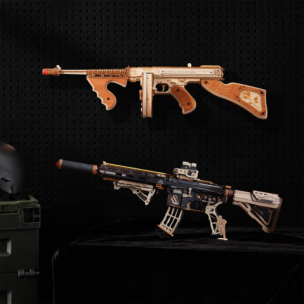 Wooden Thompson style submachine gun model mounted above a black and tan modern rifle model on a dark pegboard with a helmet.