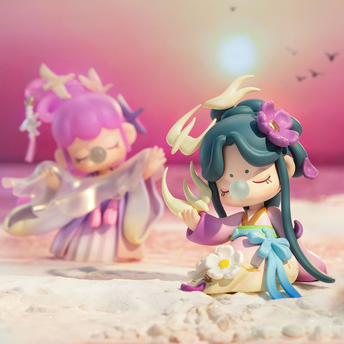 Two Rolife Nanci Poetic Beauty dolls posed on sandy shore at sunset, featuring purple winged and teal floral variants