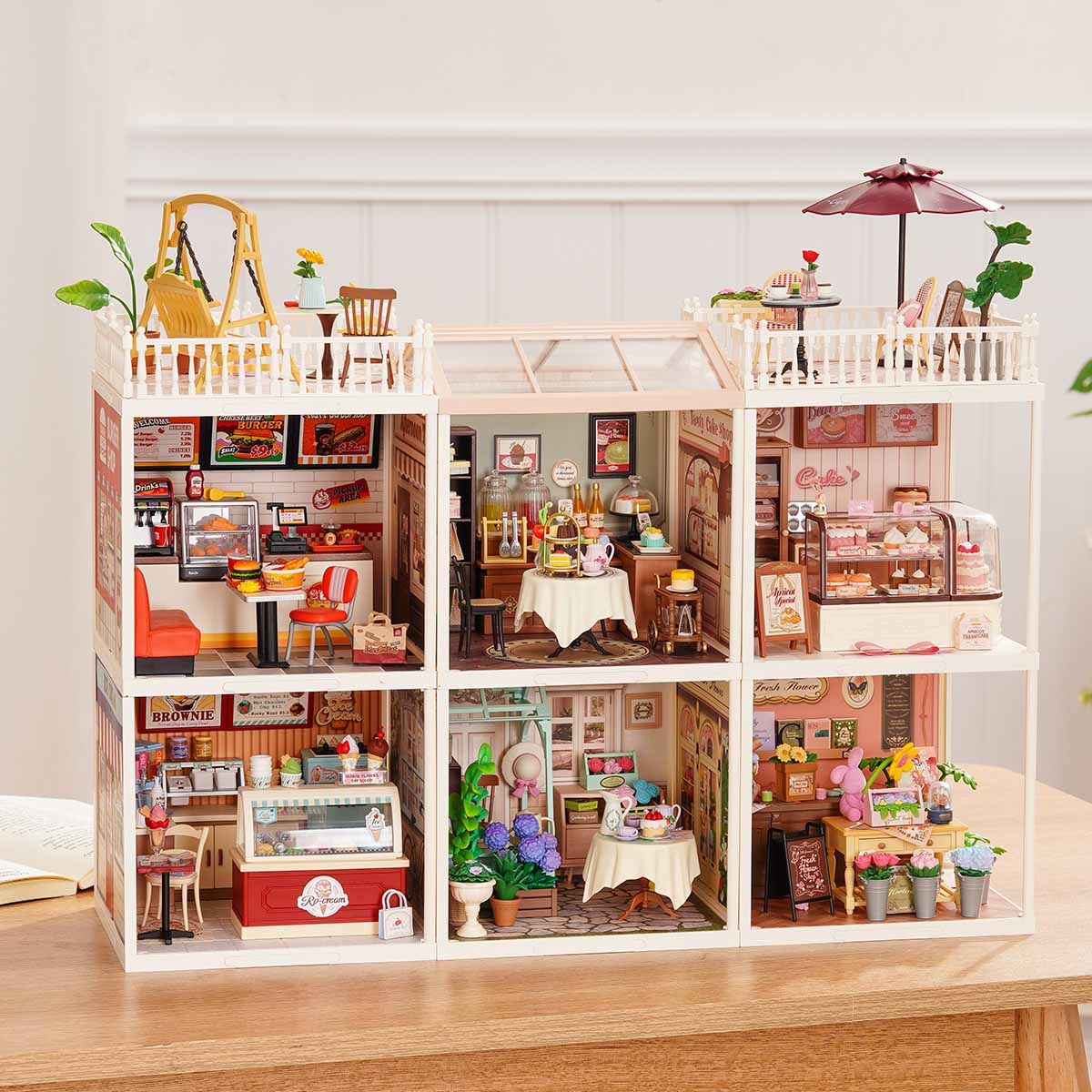 Rolife Super Creator Series 6-in-1 Six Grid miniature with six modules including cake shop, ice cream bar, bedroom, living room study, bathroom, and flower shop in a wide white frame on a table.