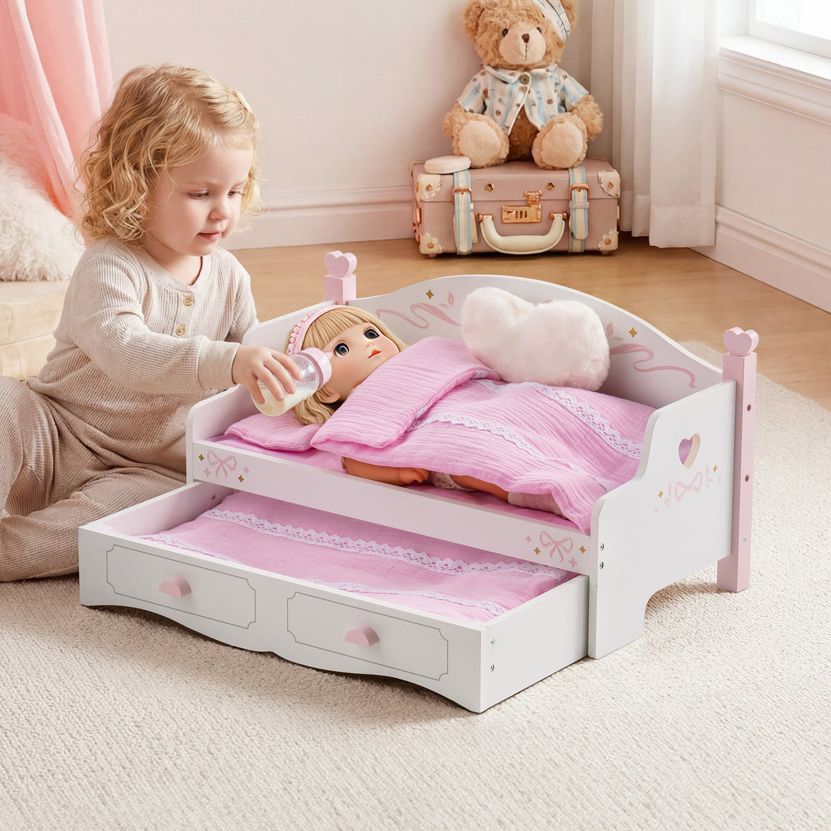 Toddler girl placing baby doll into ROBUD white and pink wooden doll sofa bed with pink quilt in a soft pink bedroom setting