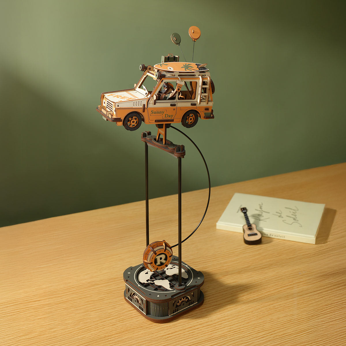 ROKR Road Tripper MCD03 lifestyle scene showing the assembled orange station wagon balanced on the pendulum stand on a wooden desk beside books