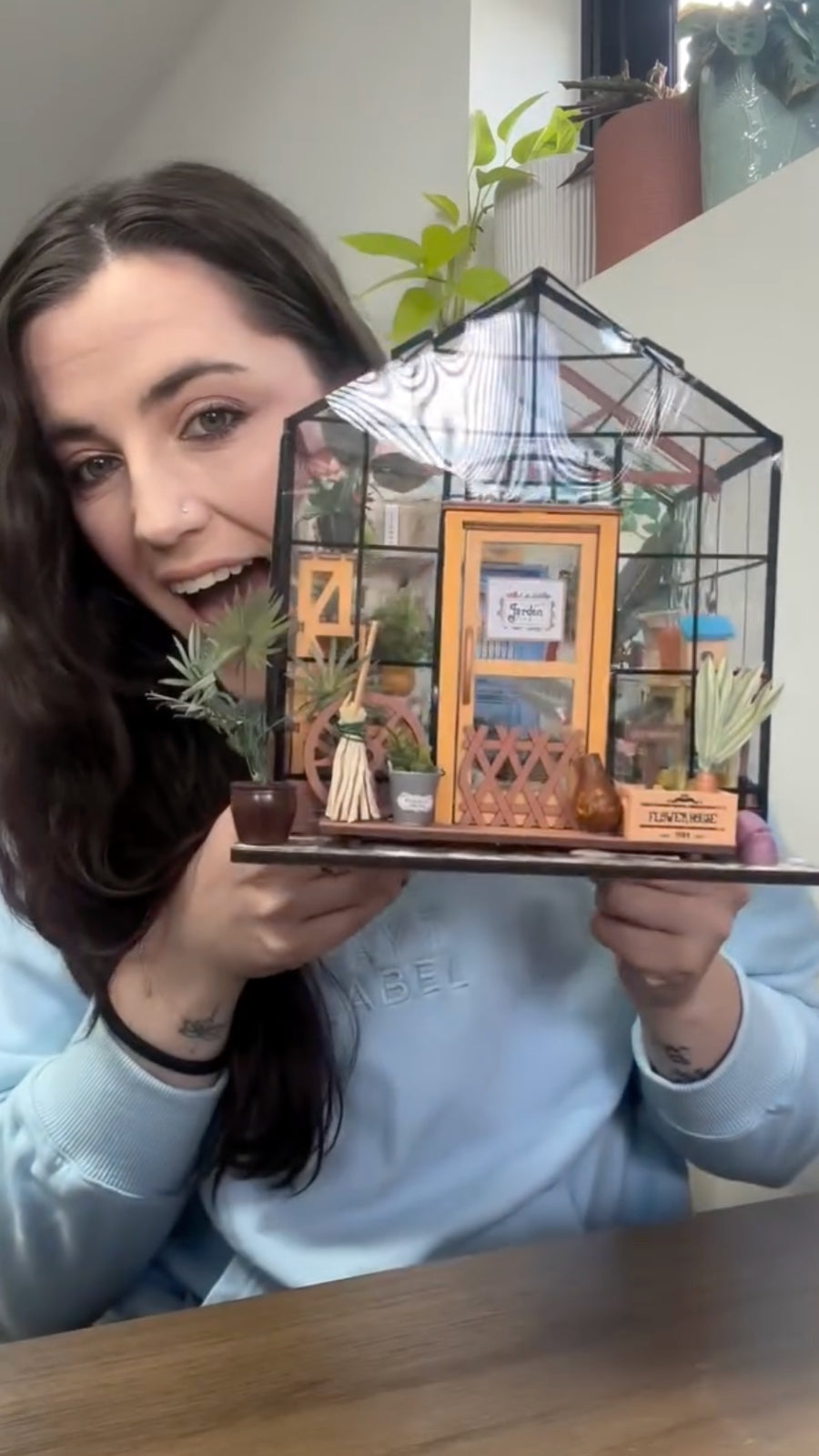 Smiling woman presenting a glass greenhouse miniature filled with plants and framed art