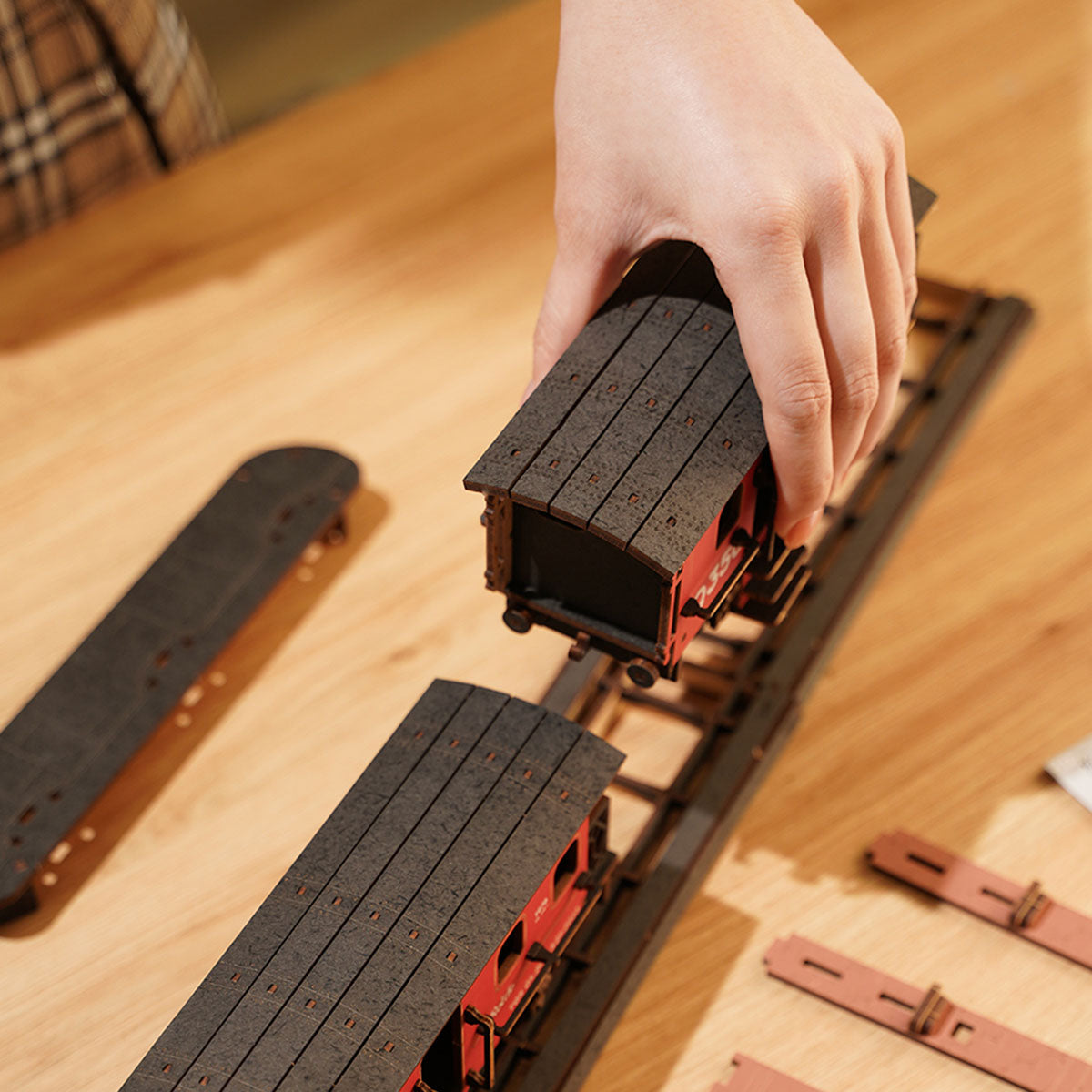 Rolife Steam Journey assembly shows a hand placing the train on wooden base panels.