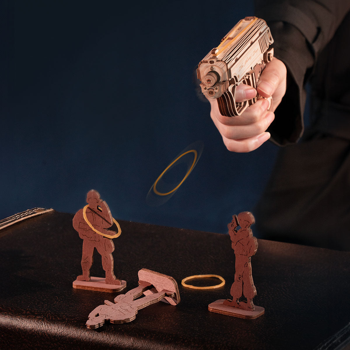 Hand holding a wooden mini gun puzzle while a rubber band launches toward small targets.