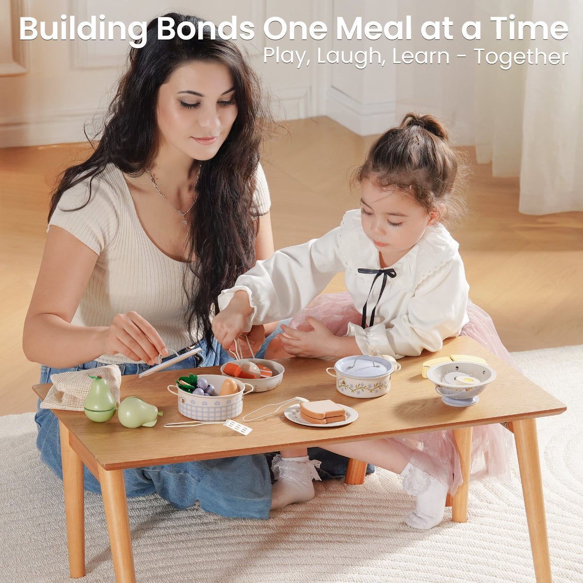 Mother and daughter sit together at a small wooden table playing with ROBUD tinplate cooking utensils and toy bowls.