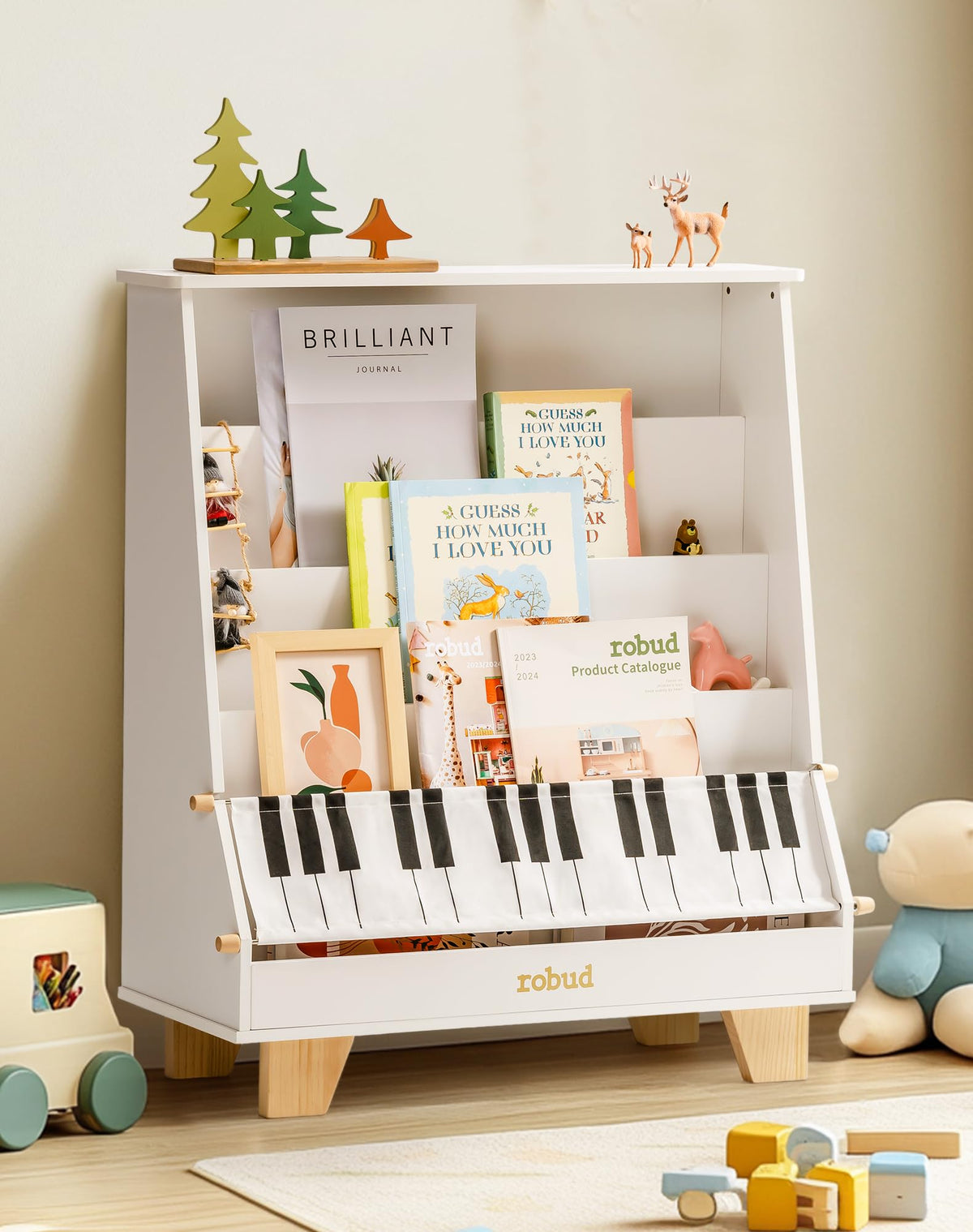 ROBUD Wooden Kids Bookshelf Piano WF009 white version in a room with wooden toys on the floor showing the tiered front-facing book display with picture books and the piano-key fabric storage pocket