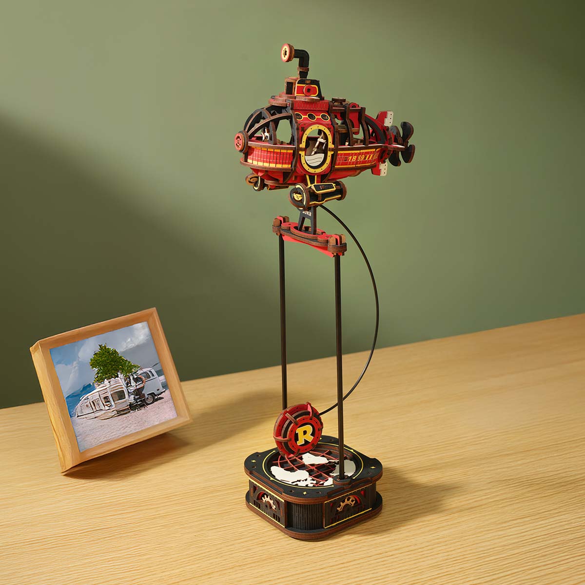 ROKR Deep-Sea Adventurer MCD04 lifestyle desk scene showing the red submarine balanced on the black pendulum stand beside a travel photo frame