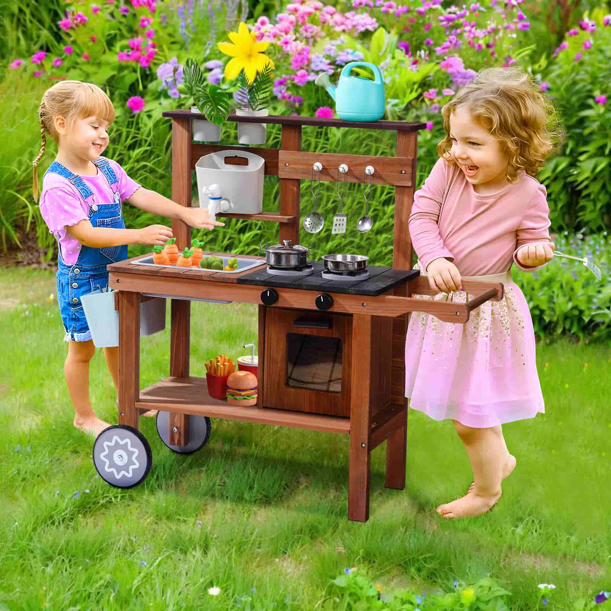 Two girls playing together at a ROBUD outdoor wooden mud kitchen surrounded by blooming flowers in a garden