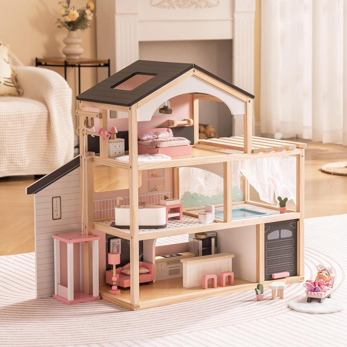 Robud three-story pink wooden dollhouse lifestyle shot placed on a rug with a baby doll resting in a lounge chair beside it