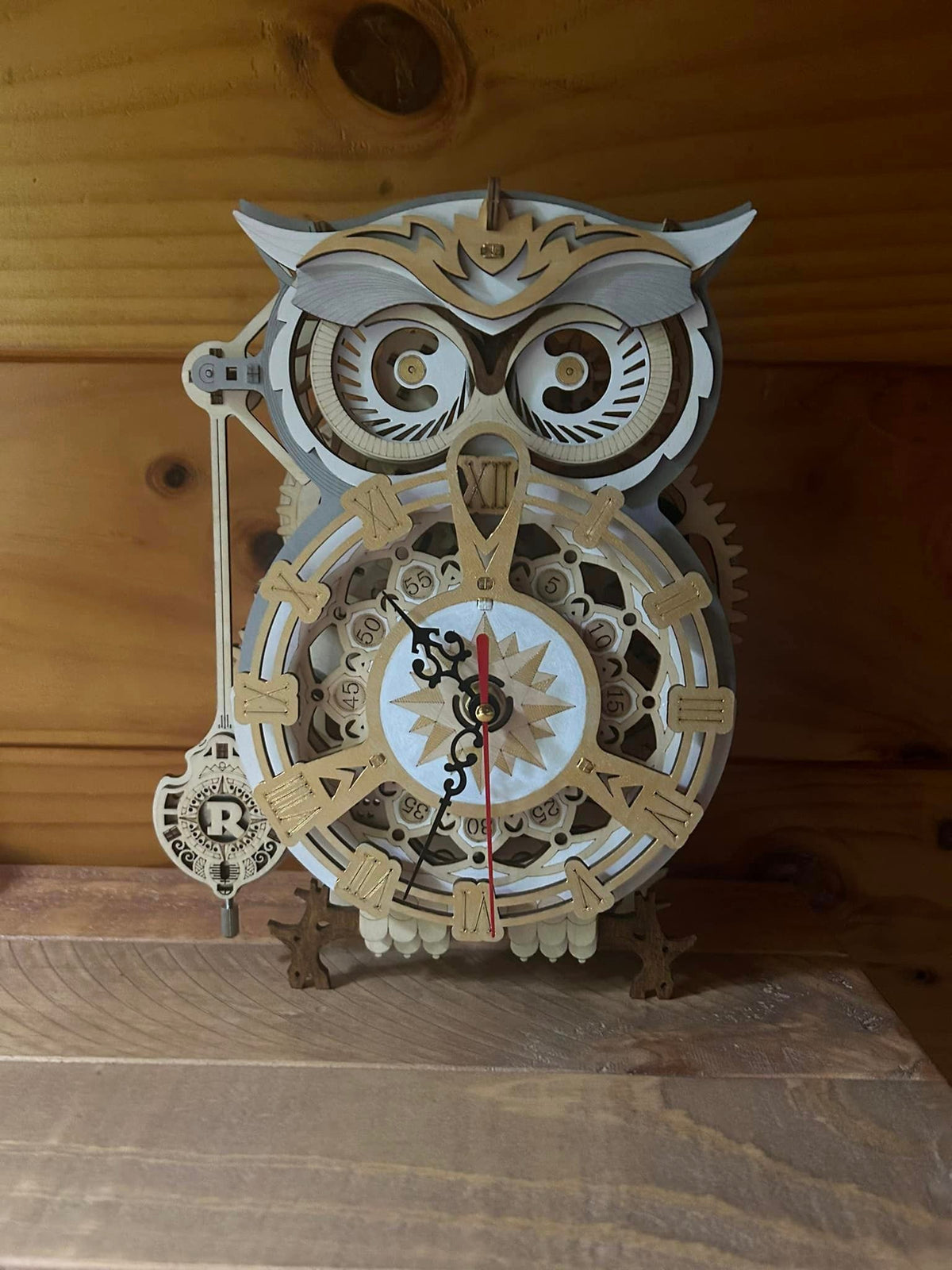 Owl shaped wooden mechanical clock with gears and a small pendulum on a tabletop.