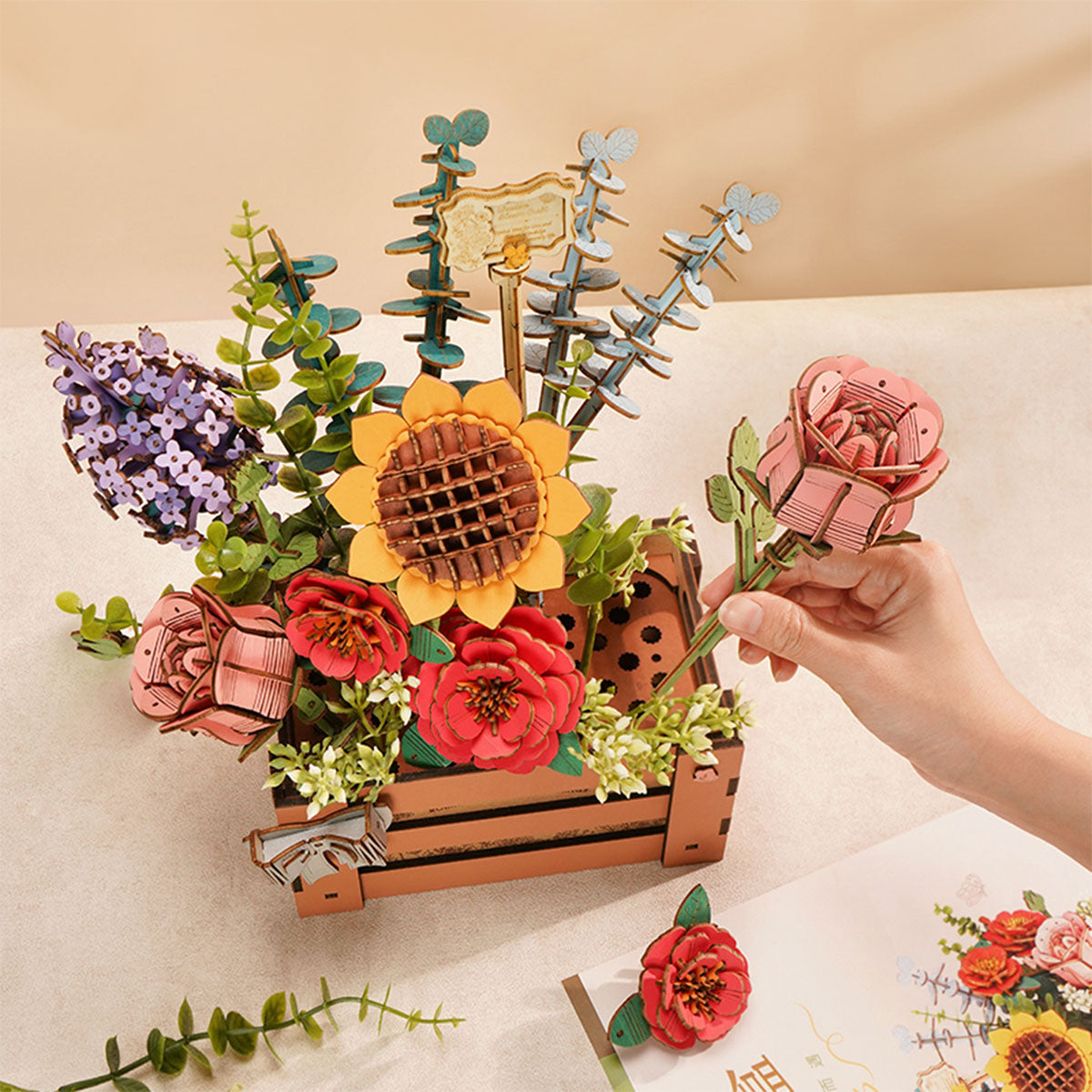 Hand placing a wooden flower stem into Rowood Wooden Bloom Box crate filled with roses and lavender