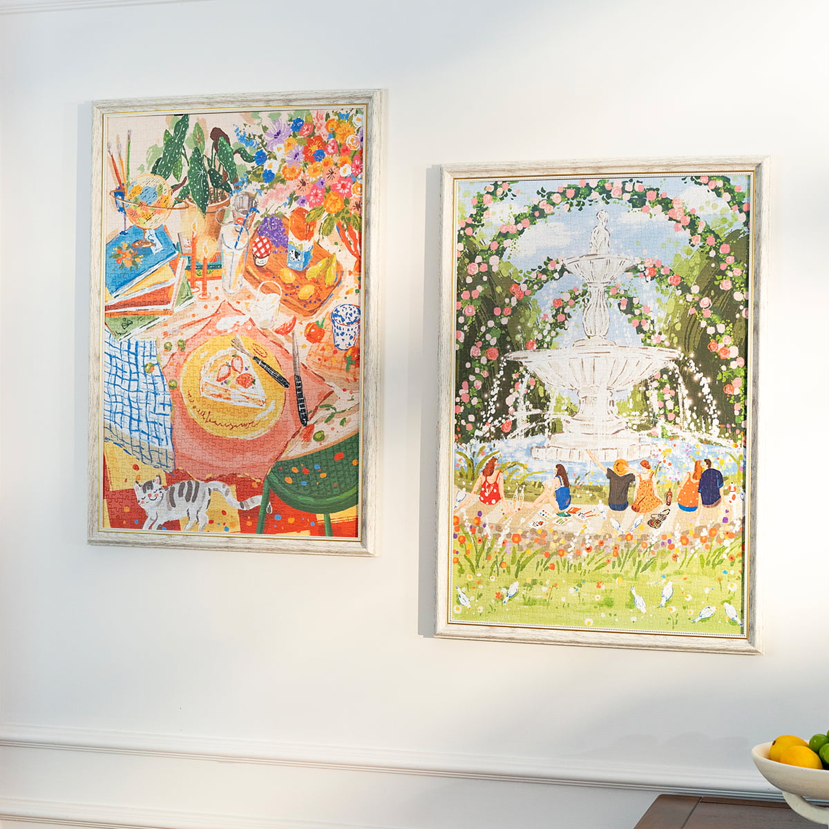 Two Rolife Leisurely Holiday and Afternoon Fountain jigsaw puzzles framed and hung on a white wall above a kitchen counter