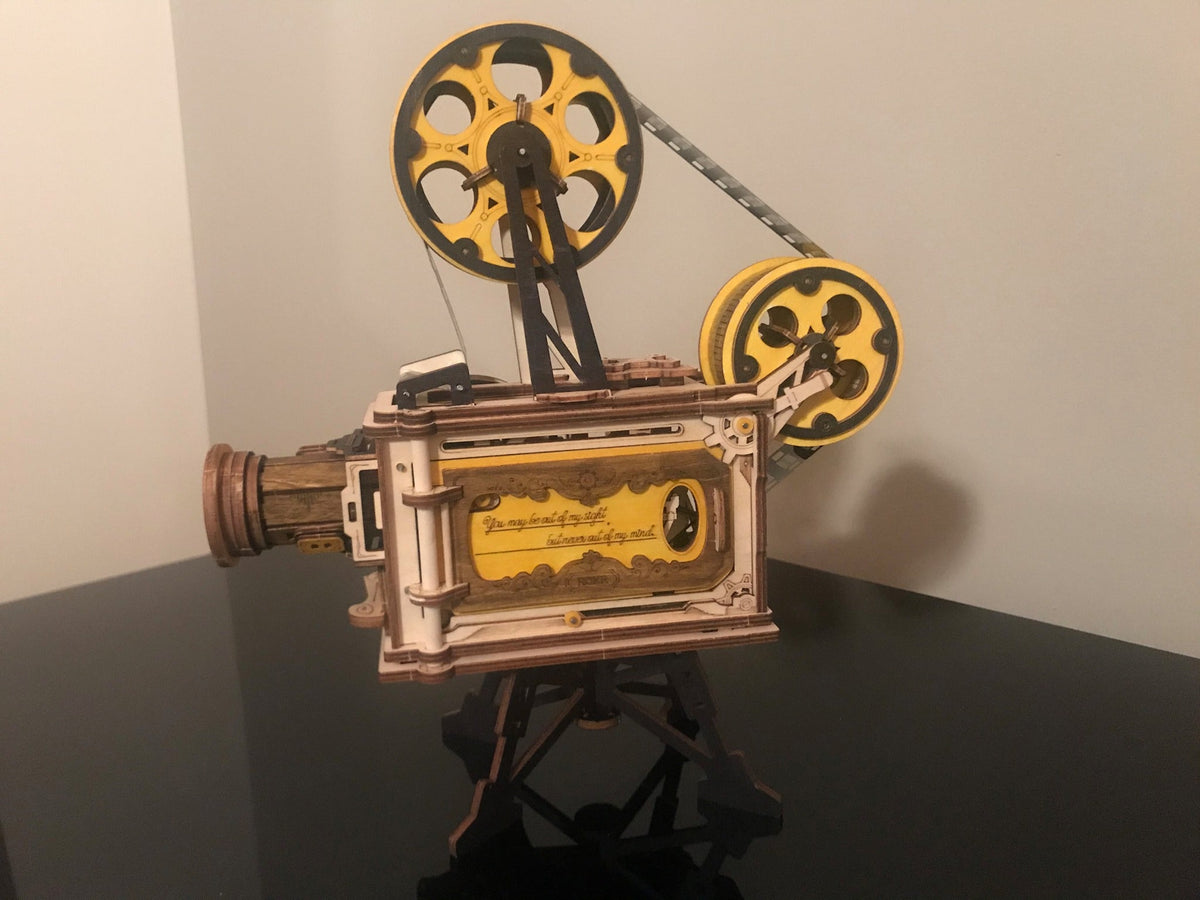 Robotime film projector music box has gold reels and a black stand in warm light.