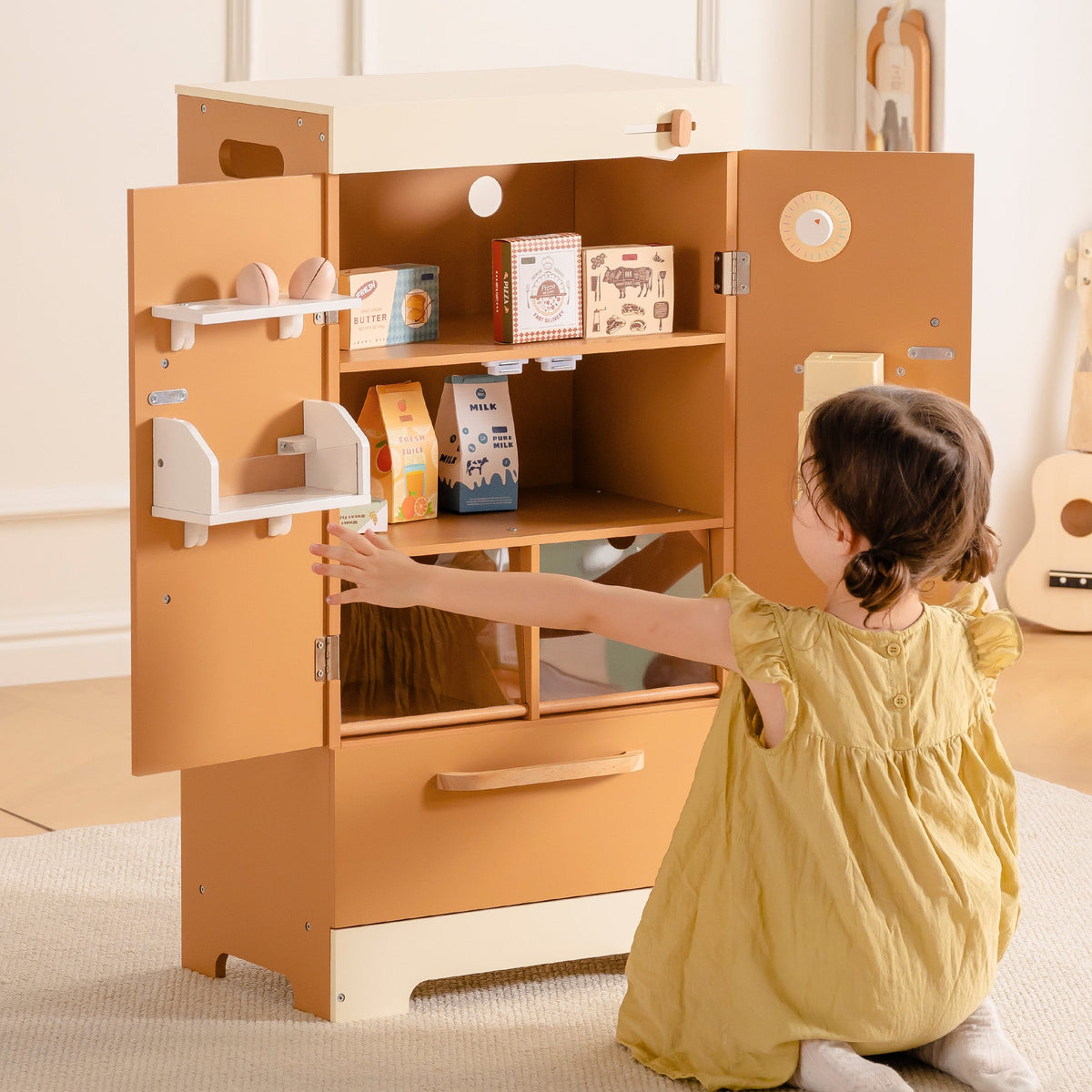 Young child in yellow dress exploring ROBUD Wooden Caramel Refrigerator with open door revealing play food items inside