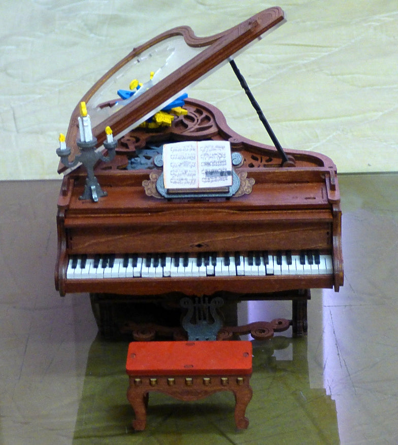 Robotime grand piano music box has a raised lid, keyboard, and red bench.
