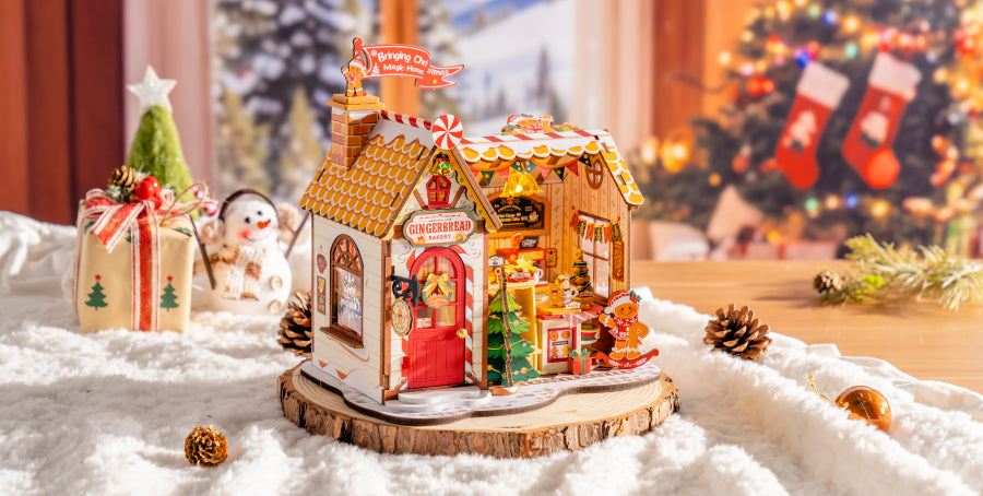 Robotime DIY miniature Christmas house with warm interior lighting on a snowy wooden display with pine cones