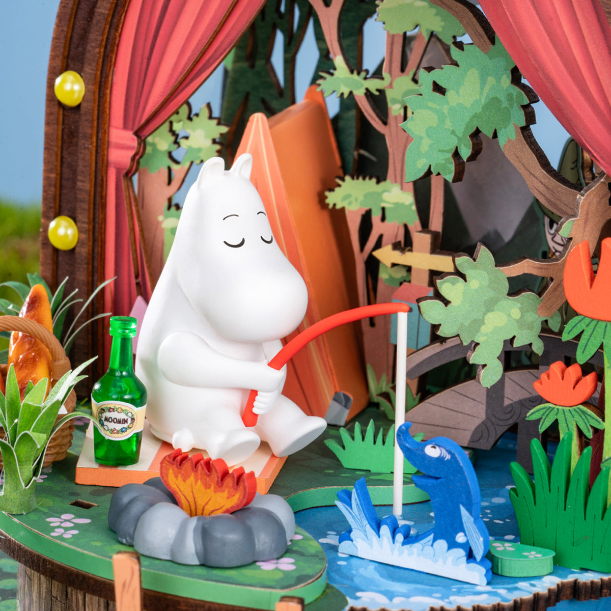 Moomintroll sits beside a campfire amid trees in the Forest Camp miniature scene