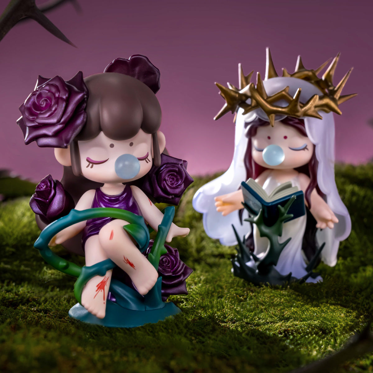 Two figurines with rose and thorn crowns seated on mossy ground against a purple night backdrop