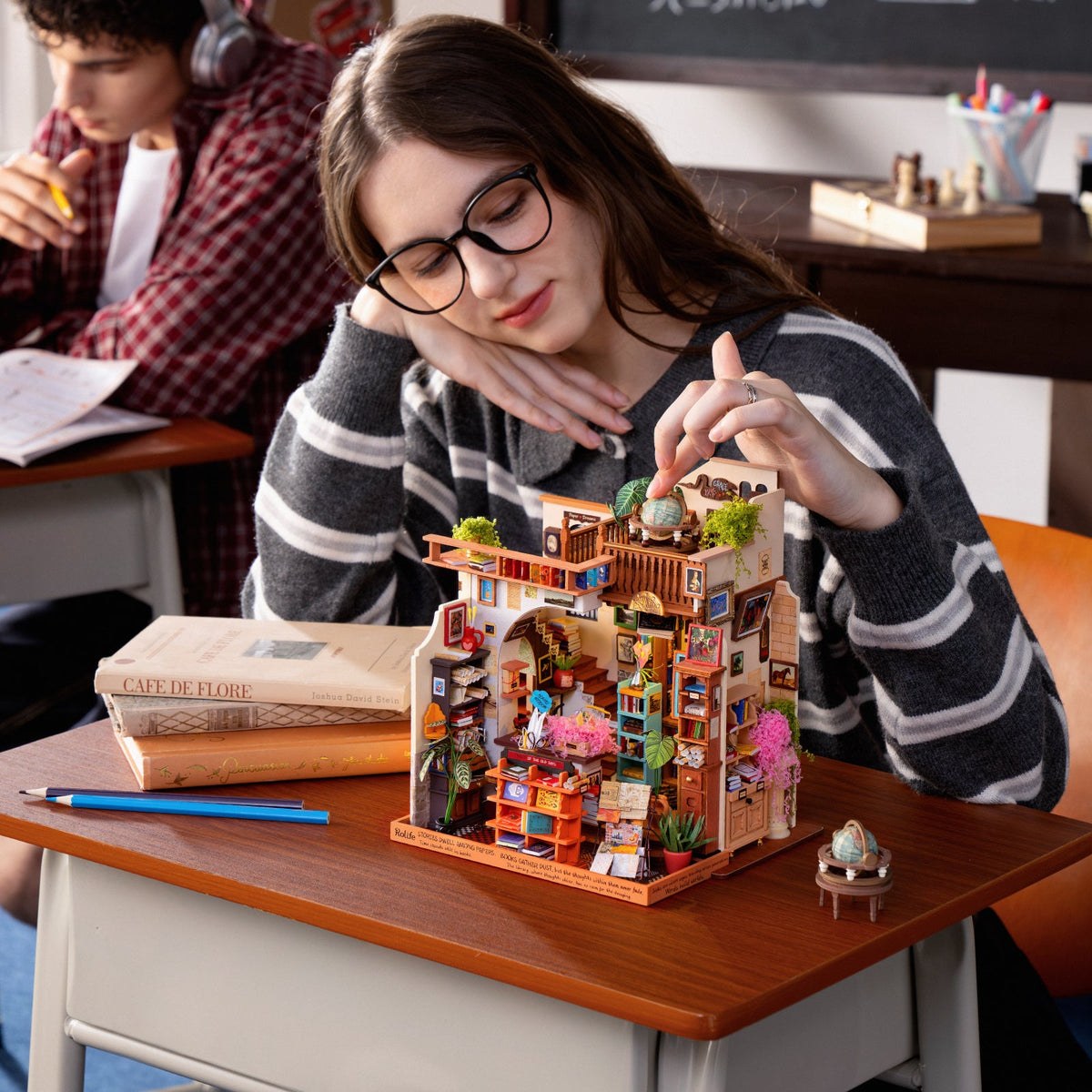 Woman placing a tiny rooftop detail on the PageStory Books miniature at her school desk