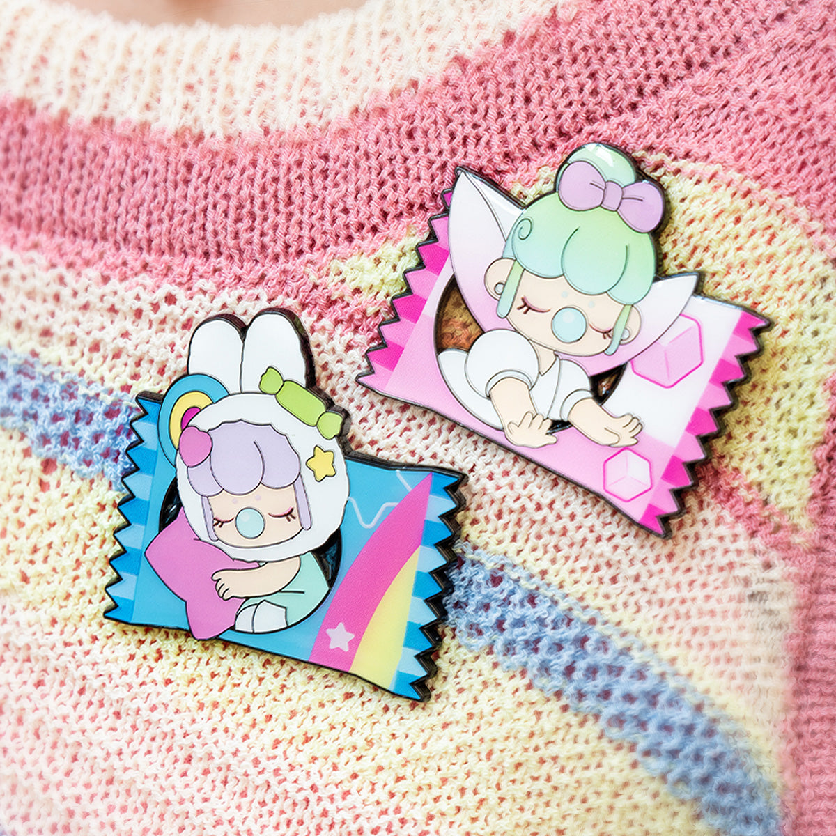 Two Rolife Nanci Sweet Time enamel pins on a rainbow-striped knit sweater displaying the Fluffy Cloud blue candy wrapper and the Tea Cup pink candy wrapper designs