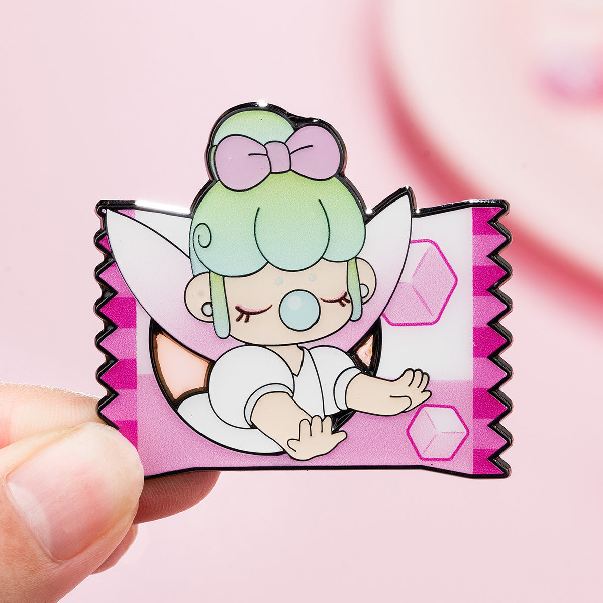 Rolife Nanci Sweet Time Tea Cup enamel pin held between two fingers showing the green-haired girl with a purple bow inside a pink candy wrapper badge