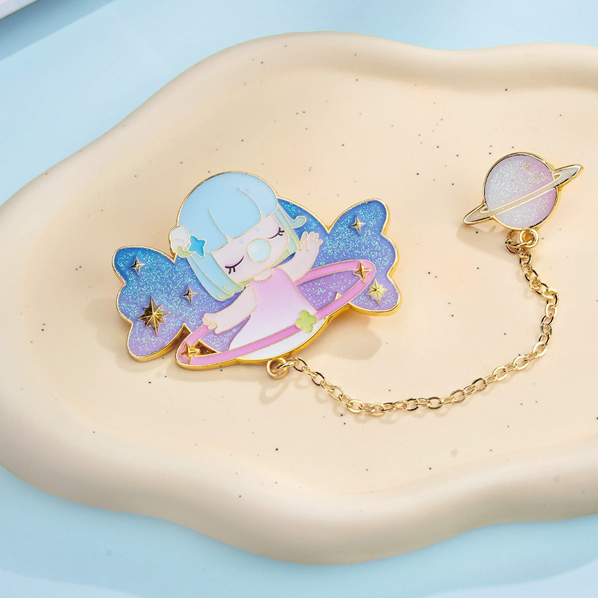 Rolife Nanci Sweet Time Badge hidden edition Honey Air enamel pin with blue glitter butterfly wings and a dangling planet charm on a gold chain, resting on a cream surface