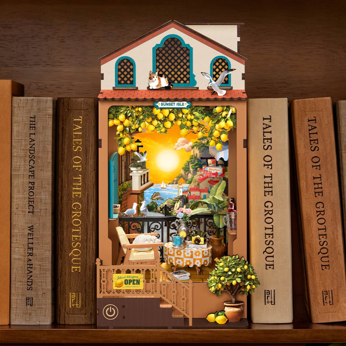 Rolife lemon garden book nook insert standing on a bookshelf between hardcover books, glowing with warm amber light inside a miniature outdoor cafe scene