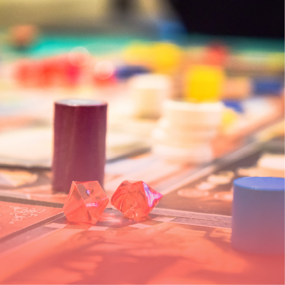 Close-up of colorful tabletop game dice and tokens on a board with warm bokeh lighting, a lifestyle category image.