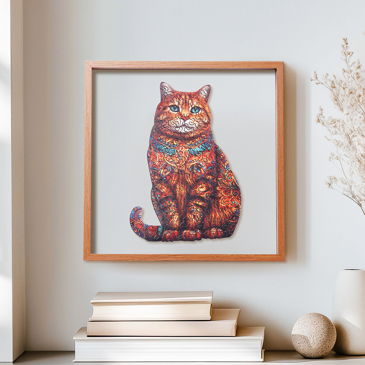 Rowood Exotic Cat orange tabby wooden jigsaw puzzle in a shadow box frame hung on a wall above stacked books and a round stone ornament