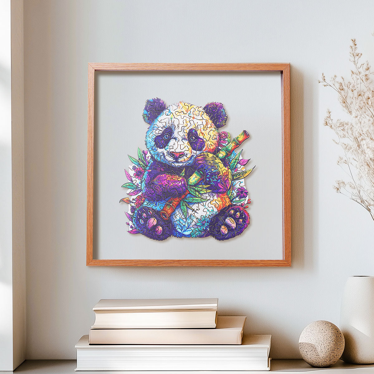 Rowood Floral Panda colorful wooden jigsaw puzzle in a shadow box frame hung on a wall above stacked books and a round stone ornament
