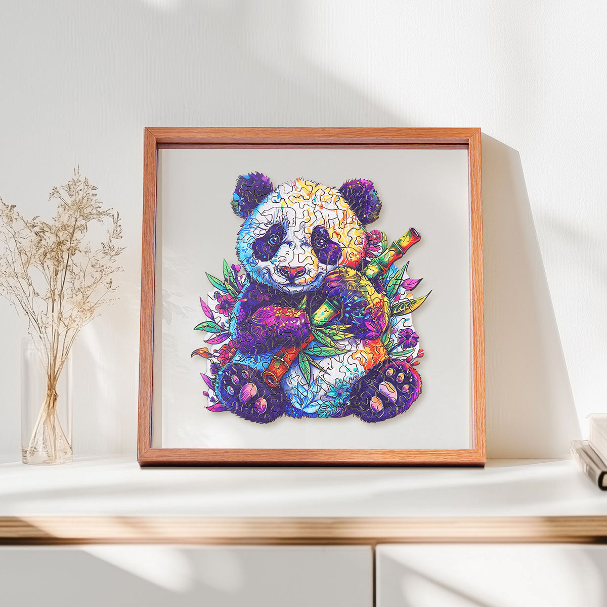 Rowood Floral Panda colorful wooden jigsaw puzzle in a shadow box frame resting on a shelf beside dried flowers and a small ceramic vase
