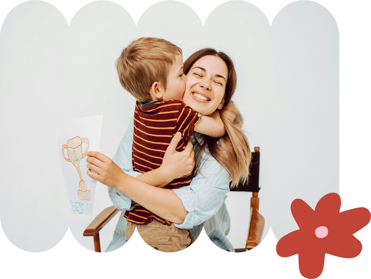 Young boy kissing his mother on the cheek as she smiles with a red flower accent on soft background