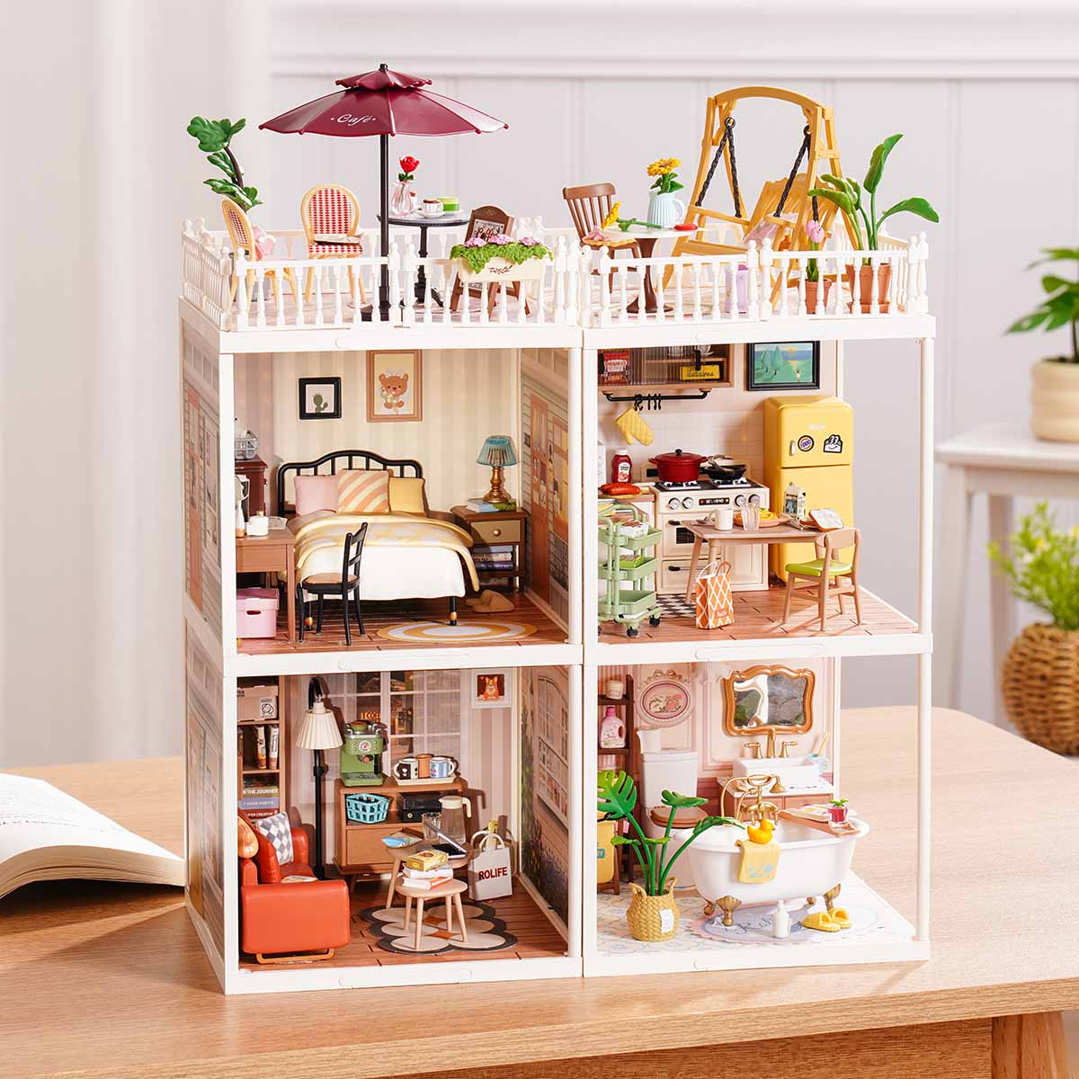 Rolife Super Creator Series 4-in-1 Four Grid modular miniature with six furnished home rooms including bedroom, flower garden, kitchen, living room, dining room, and bath in a wide white frame on a table.