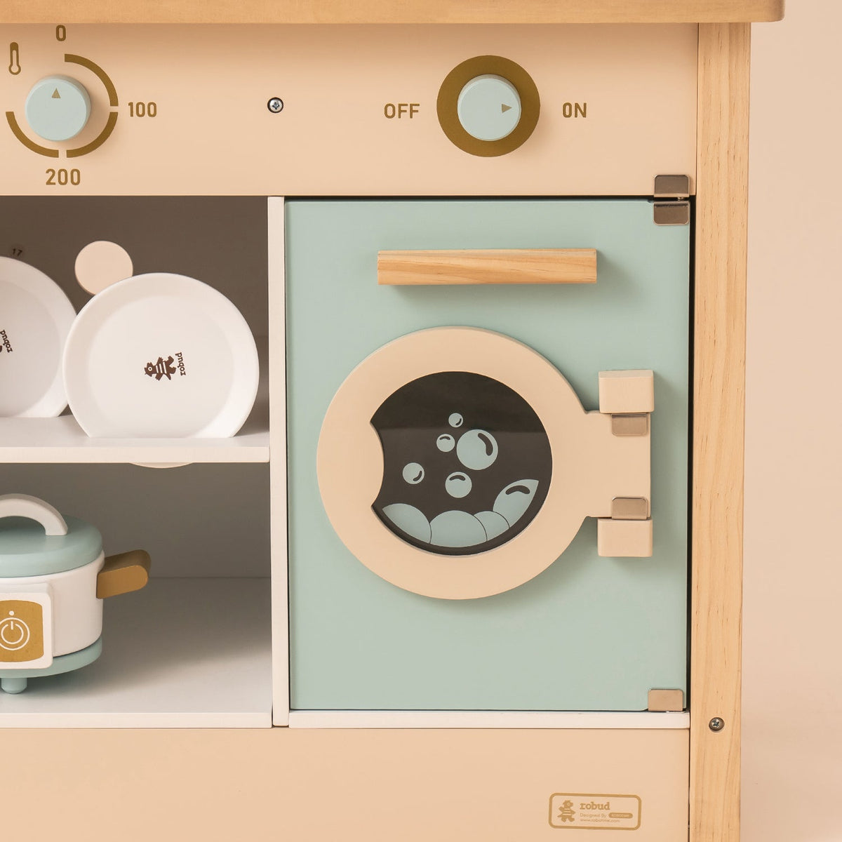 Child playing with ROBUD WCF14 mint wooden kitchen toy, kneeling and opening the washer door panel.