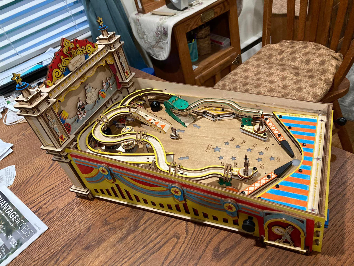 Robotime wooden pinball table has gold rails and cream playfield on a desk.
