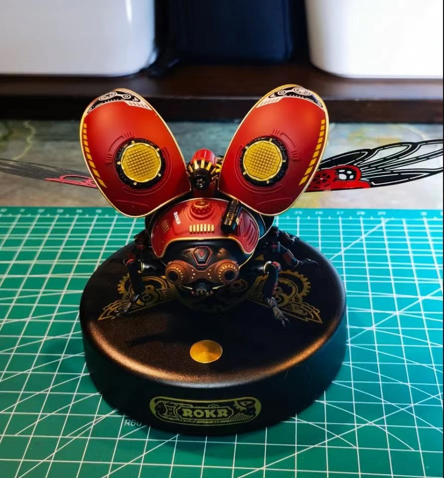 ROKR mechanical insect model with red wing covers and gold gear details on a black circular display base