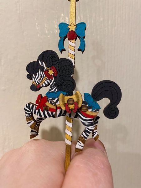 Robotime small carousel horse ornament is held in one hand against a plain wall.