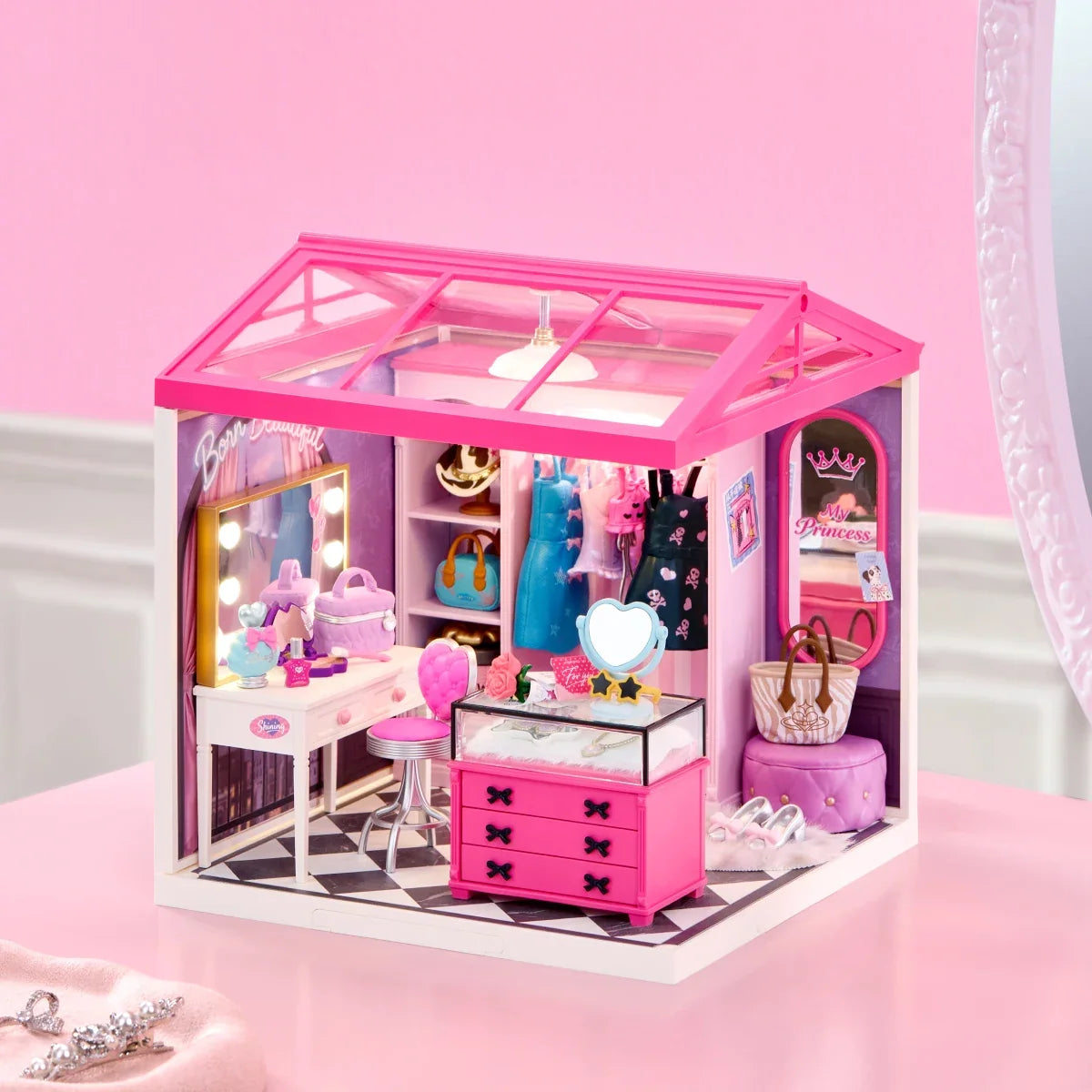 Miniatur-Ankleidezimmer mit rosa Glasdach, Schminktisch, Kleiderstange und rosa Schubladen auf einer rosa Fläche.
