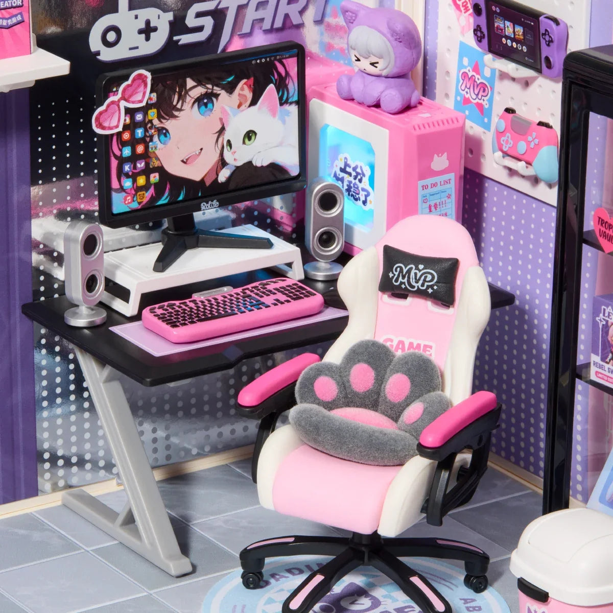 Nahaufnahme eines Miniatur-Gaming-Schreibtischs mit rosa Tastatur, Monitor mit Anime-Figur, rosa-weißem Gaming-Stuhl mit Pfotenkissen und Lautsprechern.